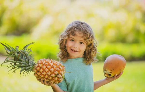 Portret van een klein kind buiten in de zomer. Glimlachend schattig grappig jongen met een ananas en kokosnoot. — Stockfoto