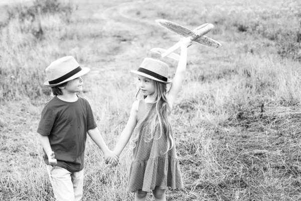 Happy childhood. Concept of dreams and travels. Enjoying nice weekend together. Two happy children boy and girl playing with toy airplane over meadow having fun and smiling. — Stock Photo, Image
