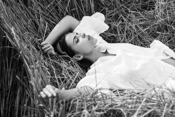 Mulher sensual deitada no feno. Menina de camisa branca e se deita em um palheiro. Retrato feminino no campo no campo. — Fotografia de Stock