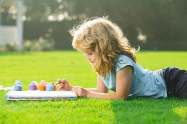Çocuk resimleri. Çocuk parkta resim çiziyor, resim yapıyor. Küçük ressam açık havada resimler çizer..