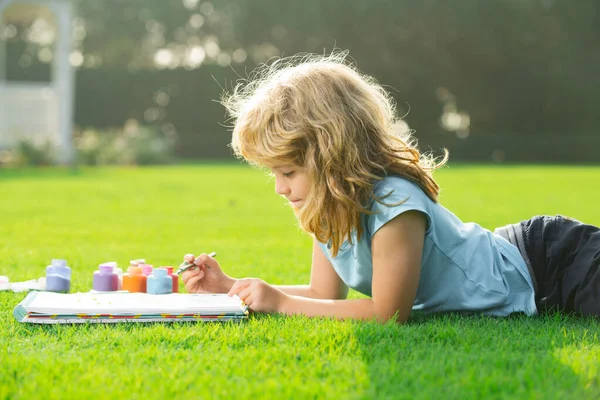 Gyerekrajzok. Gyerek fiú rajzol a nyári parkban, festi a művészetet. Kis művész festő rajzol képeket szabadban. — Stock Fotó