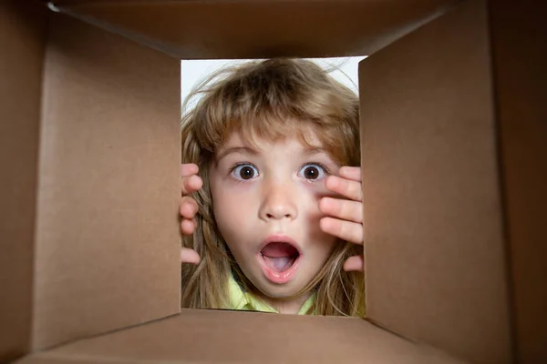 El niño sorprendido desempacando, abriendo la caja de cartón y mirando dentro. El paquete, entrega, sorpresa, concepto de regalo para niños. Primer plano niños cara. Fotos de stock libres de derechos