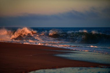 Deniz dalgaları arka planı. Günbatımında deniz manzarası ve tropikal plaj ya da tatil ve tatil için gün doğumu. Sudaki güneşin yansıması ve kumsaldaki kum. Dalgalar sıçrıyor.