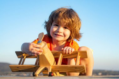Tahta uçaklı küçük çocuk, pilot ve astronot olmak istiyor. Mutlu çocuk oyuncak uçakla oynuyor. Çocuklar uçmayı hayal eder. Tatlı çocuk suratı..