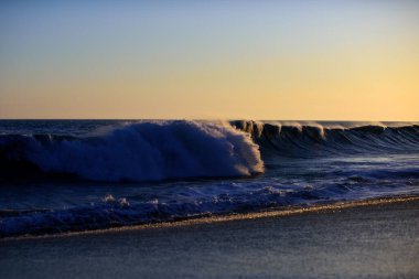 Dalgalar sıçrıyor. Altın dramatik gökyüzü manzaralı deniz üzerinde gün batımı. Okyanus dalgaları arka planı. Okyanus ve gökyüzü arkaplanı.