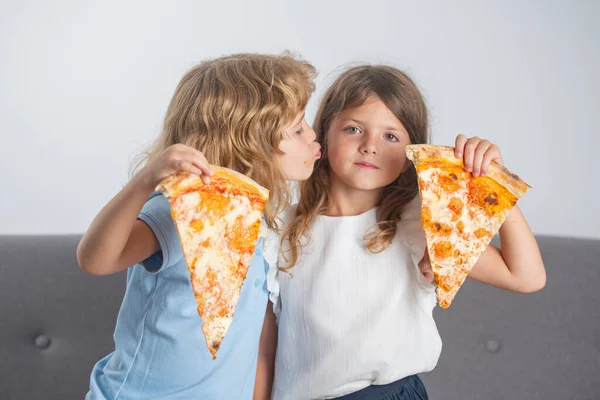 Hungry kids eating pizza. Happy children eating pizza and having fun together. Happy kids holding pizza slice near face and kissing. — Stock Photo, Image
