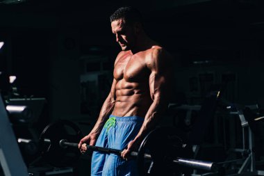 Spor adamı halter kaldırarak biceps yapıyor. Dambılı tişörtü olmayan atletik bir adamın portresi. Gövdesi kaslı, tişörtsüz bir adam spor salonunda..