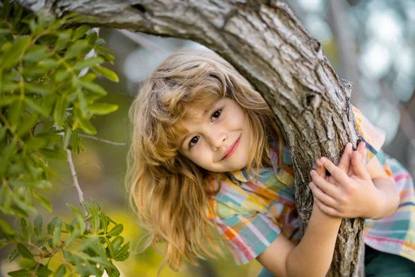 Carino il ragazzino che si diverte ad arrampicarsi sull'albero il giorno d'estate. Ragazzo felicemente sdraiato su un albero che abbraccia un grosso ramo. — Foto Stock