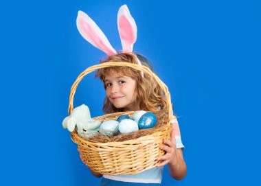 Mutlu Paskalyalar. Paskalya sepeti olan çocuk mavi arka planda izole edilmiş. Komik çocuk suratı.