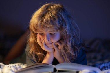 Yatakta uzanmış kitap okuyan sevimli bir çocuk. Çocuk yatmadan önce kitap okuyor. Hayal gücü ya da öğrenme kavramı.