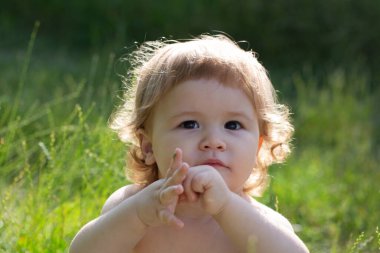 Bebek yüzlü, yakın çekim. Küçük komik çocuk portresi. Sarışın çocuk, duygusal yüz. Yaz parkında çimlerin üzerinde bebek.