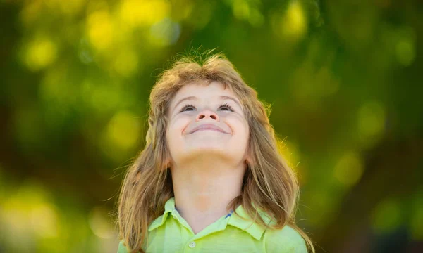 Közelkép egy cuki fiúról, aki a szabadban néz fel. Szoros fejlövés portré mosolygós kisfiú a természet hátterében, boldog kis óvodás gyermek. — Stock Fotó
