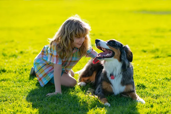 Happy kid and pet dog playing at backyard lawn. Child with pet puppy dog. Happy smiling kid with pets best friend, sitting on grass. Cute dog. — Stock Photo, Image