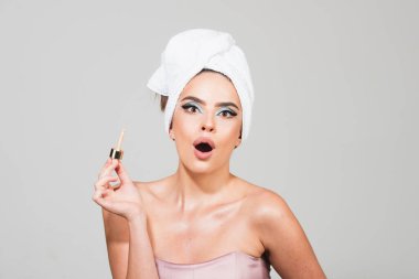 Kafasında havlu, makyaj ve kozmetik ürünleri olan güzel bir kadın. Mükemmel yüz derisi ve parlak makyaj portresi olan kız model..