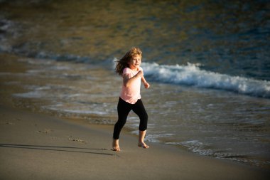 Okyanus boyunca koşan küçük bir çocuk. Çocuk kumsalda koşuyor. Çocukla yaz tatili.