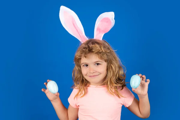 Retrato de niño en orejas de conejo cazando huevos de Pascua al aire libre. Niño que tiene pascua aislada sobre fondo azul. —  Fotos de Stock