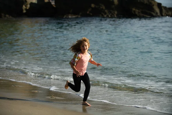 Niño feliz corriendo en la playa del mar. Chico gracioso corre a lo largo del borde del surf. Estilo de vida de niños activos. Carrera y deporte saludable para los niños. —  Fotos de Stock