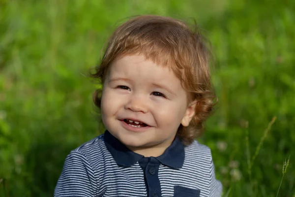 Porträtt av en liten pojke som leker utomhus i gräset. Baby ansikte på nära håll. Lustigt litet barnporträtt. Blond unge, känslomässigt ansikte. — Stockfoto