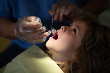 Doktora sözlü muayene sırasında ağzı açık bir şekilde dişçi koltuğunda oturan tatlı çocuk. Dişçi muayenehanesi. Çocukların stomatolojisi. Ağız boşluğu.