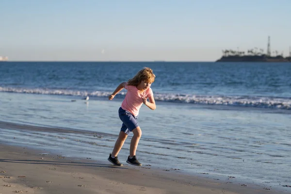 ビーチで遊んでいる子供たち。子供たちは夏休みに海で遊ぶ。砂と水の楽しさ、太陽の保護。海の岸を走って飛び跳ねる小さな子供. — ストック写真