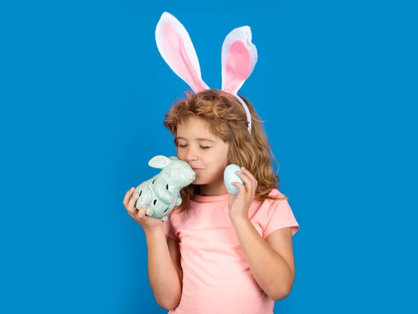 Niña conejita. Niño cazando huevos de Pascua. Niño con huevos de Pascua y orejas de conejo aisladas sobre fondo azul. Cara divertida de los niños. —  Fotos de Stock