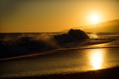 Dalgalar sıçrıyor. Deniz dalgaları arka planı. Altın dramatik gökyüzü manzaralı deniz üzerinde gün batımı. Gün batımı gökyüzü olan sakin bir deniz. Okyanus ve gökyüzü arkaplanı. Altın gökyüzü ve okyanus suyu.