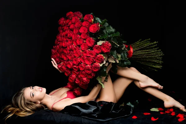 Красивая женщина с цветочком розы, красивая модница, портрет на голове. Красивая соблазнительная женщина с большим букетом красных роз на черном фоне. День Святого Валентина. — стоковое фото
