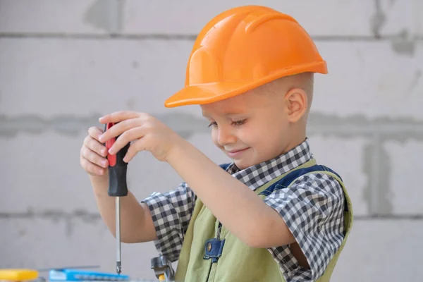 Kind spelen met benodigdheden, gereedschap zaag, hamer, schroevendraaier, helm, bouwer, timmerman. Kinderen die in het vak spelen. Kleine reparateur. Kid jongen in bouwers uniform en helm met reparatie gereedschap. — Stockfoto