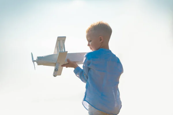 Niño jugando con un avión de juguete de madera, sueña con convertirse en piloto. Sueños de niños. Aviador piloto infantil con avión de madera. Concepto de imaginación de sueño infantil. — Foto de Stock