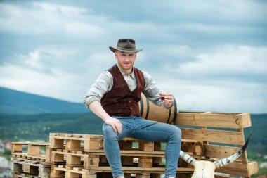 Kovboy çiftçisi kovboy şapkası takarak viski içer. Çiftliğin kırsal kesiminde Amerikan erkek modeli.