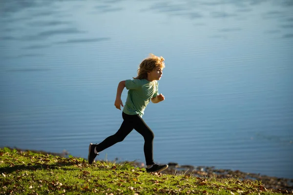 Ungarna springer utomhus. Sportig liten barn jogging och träning utomhus. Barn springer på sommarfält nära sjön, barn fitness. — Stockfoto