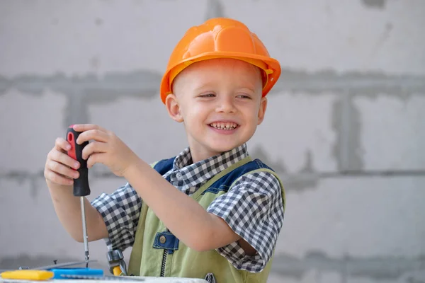 Мальчик держит отвертку. Счастливый улыбающийся ребенок крутит болт с отвёрткой. Маленький ремонтник с ремонтным инструментом. Симпатичный ребенок строитель. Дети играют с отверткой. — стоковое фото