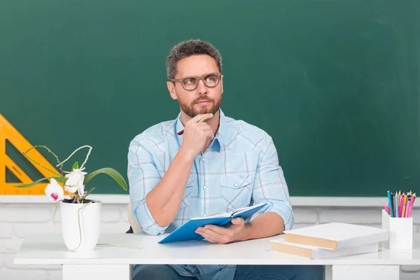 男教师在思考聪明的年轻导师戴眼镜和书本的画像，在课堂上挂在黑板上，或者是拼贴在墙上。大学生中的男生. — 图库照片