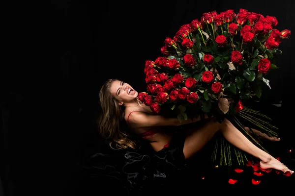 Sensuell kvinna med röda läppar med röd ros, svart bakgrund. Vacker sexig kvinna som håller stor bukett röda rosor på svart bakgrund. Alla hjärtans dag. Semester födelsedag dag. — Stockfoto