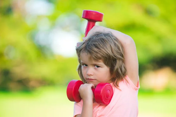 Sport kind jongen met sterke biceps spieren. Kinderen die fitness halters trainen. Sterke kleine jongen aan het trainen met halter in het park. Gezonde activiteiten kids levensstijl. — Stockfoto