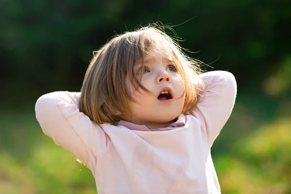 Verrast kind meisje in gras op de fieald op zonnige zomeravond. Emotioneel babygezicht. — Stockfoto