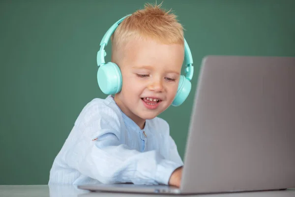 Rapaz da escola inteligente, aluno bonito usa fones de ouvido escrevendo no laptop, ouvir computador uso lição de áudio. Educação, escola, tecnologia e conceito de crianças. — Fotografia de Stock