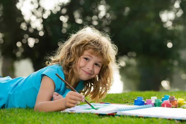 Child boy draws in park laying in grass having fun on nature background. Royalty Free Stock Images