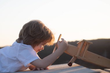 Tahta uçaklı küçük çocuk, pilot ve astronot olmak istiyor. Mutlu çocuk oyuncak uçakla oynuyor. Çocuklar uçmayı hayal eder. Çocukluk hayali kavramı.