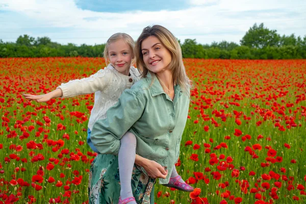 Madre e hija abrazándose en un prado de amapolas. Mamá y niña descansando en el campo con flores de amapola, paseo a cuestas. Feliz maternidad.. —  Fotos de Stock