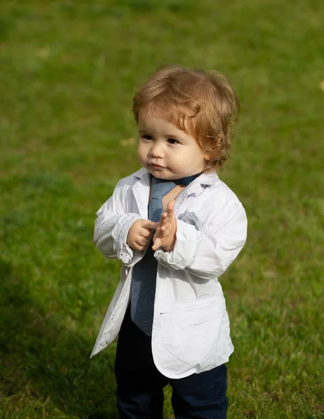 Портрет милого маленького кавказького хлопчика, який розважається в саду. Дитина на зеленому газоні під час прогулянки у дворі. Щасливе дитинство та охорона здоров'я дітей. Смішний маленький чоловік у костюмі, піджаку і краватці . — стокове фото