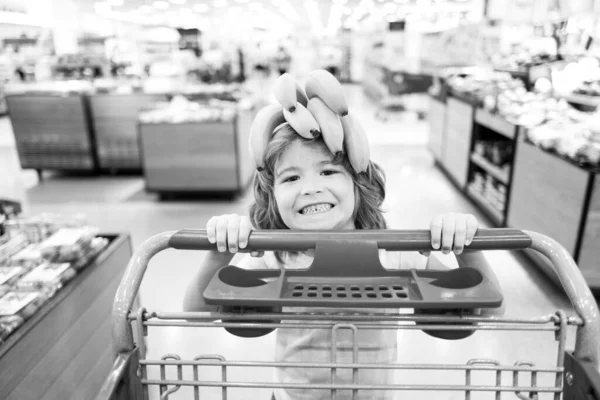 Criança com carrinho de compras na mercearia ou supermercado. Miúdo a comprar banana no mercado de mercearia. — Fotografia de Stock