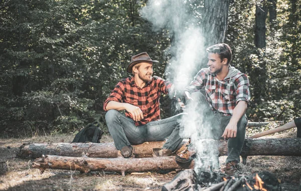 Two handsome men friends on camping near campfire. Friends men hikers watching fire together on camp. Two friends spend leisure weekend hike picnic forest nature background. — Stock Photo, Image