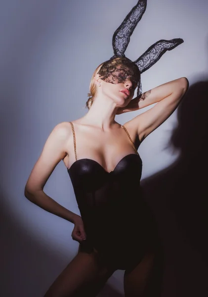 Красива сексуальна жінка з великими грудьми носить карнавальну чорну маску великоднього кролика. Блондинка позує біля сірої стіни в студії. Сексуальна кролика жінка . — стокове фото