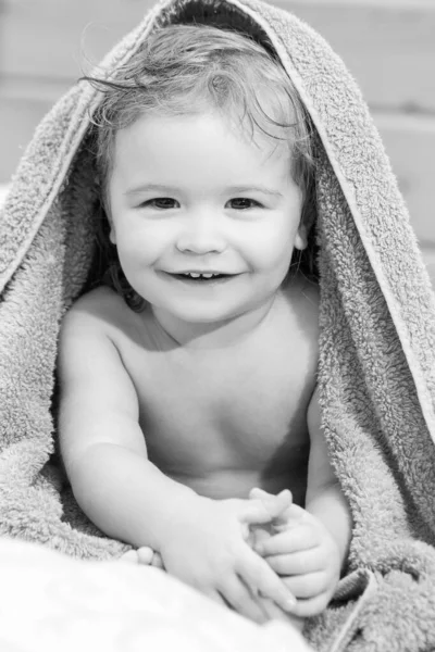 洗完澡后用毛巾把一个金发小男孩的画像贴在身上.有趣的婴儿在家里的床上洗澡后. — 图库照片