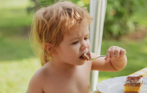 Baby taart aan het eten. Grappig schattig jongetje eet zoete taart. Kinderdessert met lepel in het park op de picknick. — Stockfoto