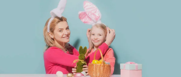 Matka a dcera slaví Velikonoce. Roztomilá holčička s legračním obličejem v králičích uších se směje, usmívá a baví se izolovaně na modré. Velikonoční nápis s kopírovacím prostorem. — Stock fotografie