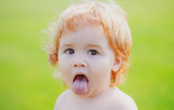 Criança engraçada no parque. Cara de bebê com língua de perto. Engraçado pequeno retrato closeup criança. Menina loira, cara de emoção. — Fotografia de Stock