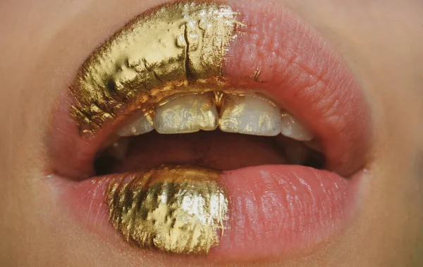 Gold lips. Gold paint from the mouth. Golden lips on woman open sensual mouth with make-up. Sensual and creative design for golden metallic.