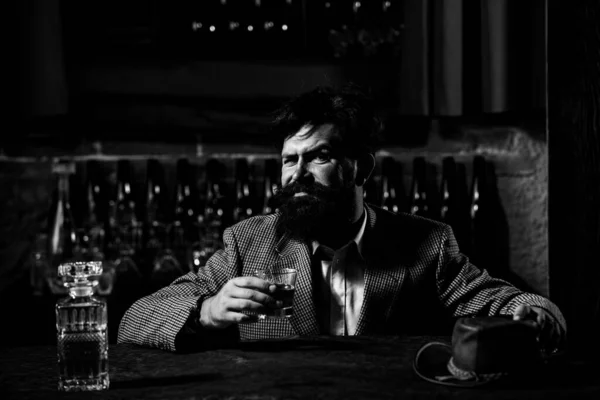 Przystojny mężczyzna trzyma szklankę whisky i odwraca wzrok siedząc w barze w domu. — Zdjęcie stockowe